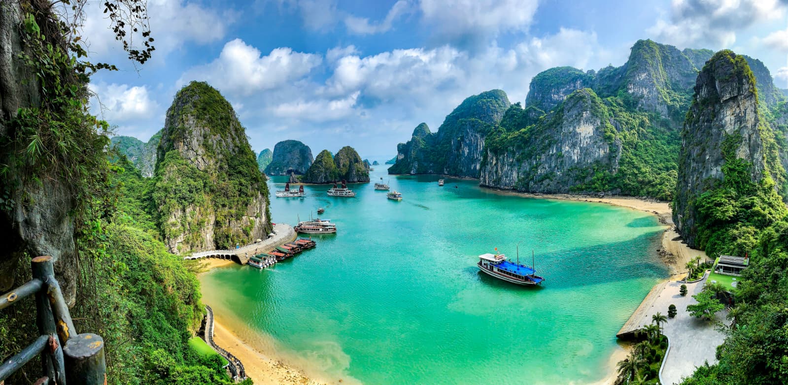 Turquoise Halong Bay dotted with boats and limestone karsts, seen from a lookout